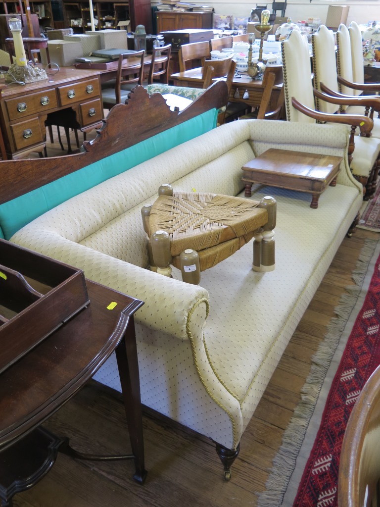 An Edwardian upholstered settee, the fully upholstered scroll back and arms on turned legs and brass