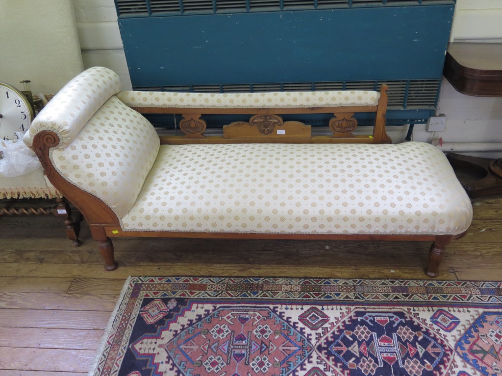 An Edwardian beech chaise longue, with scroll arm and floral carved back on turned legs