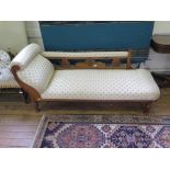 An Edwardian beech chaise longue, with scroll arm and floral carved back on turned legs
