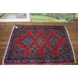 A small oriental rug, the red field with three medallions within a blue border 106cm x 73cm