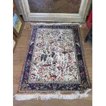 A Qum silk rug, the ivory field filled with floral trees with birds and deer, within a similar