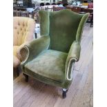 A George III green upholstered wing armchair on cabriole legs