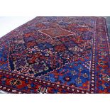 A 20TH CENTURY MIDDLE EASTERN GEOMETRIC PATTERNED RUG on red ground with blue repeating flowers