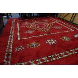 A 20TH CENTURY MOROCCAN RED GROUND RUG of geometric pattern design and fringed edges, 300cm x 206cm