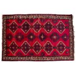 A MID TO LATE 20TH CENTURY MIDDLE EASTERN RED GROUND RUG with three rows of diamond motifs and a