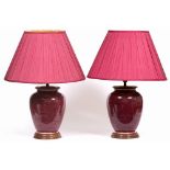 A PAIR OF RED GLAZED OVOID POTTERY TABLE LAMPS with turned wooden bases and pleated silk shades 62cm