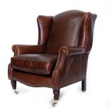 A BROWN LEATHER UPHOLSTERED WING BACK ARMCHAIR with turned fluted front legs and brass castors