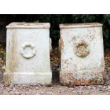 A PAIR OF WHITE PAINTED TERRACOTTA URN PLINTHS each decorated with wreaths of ribbon tied reeds 34cm