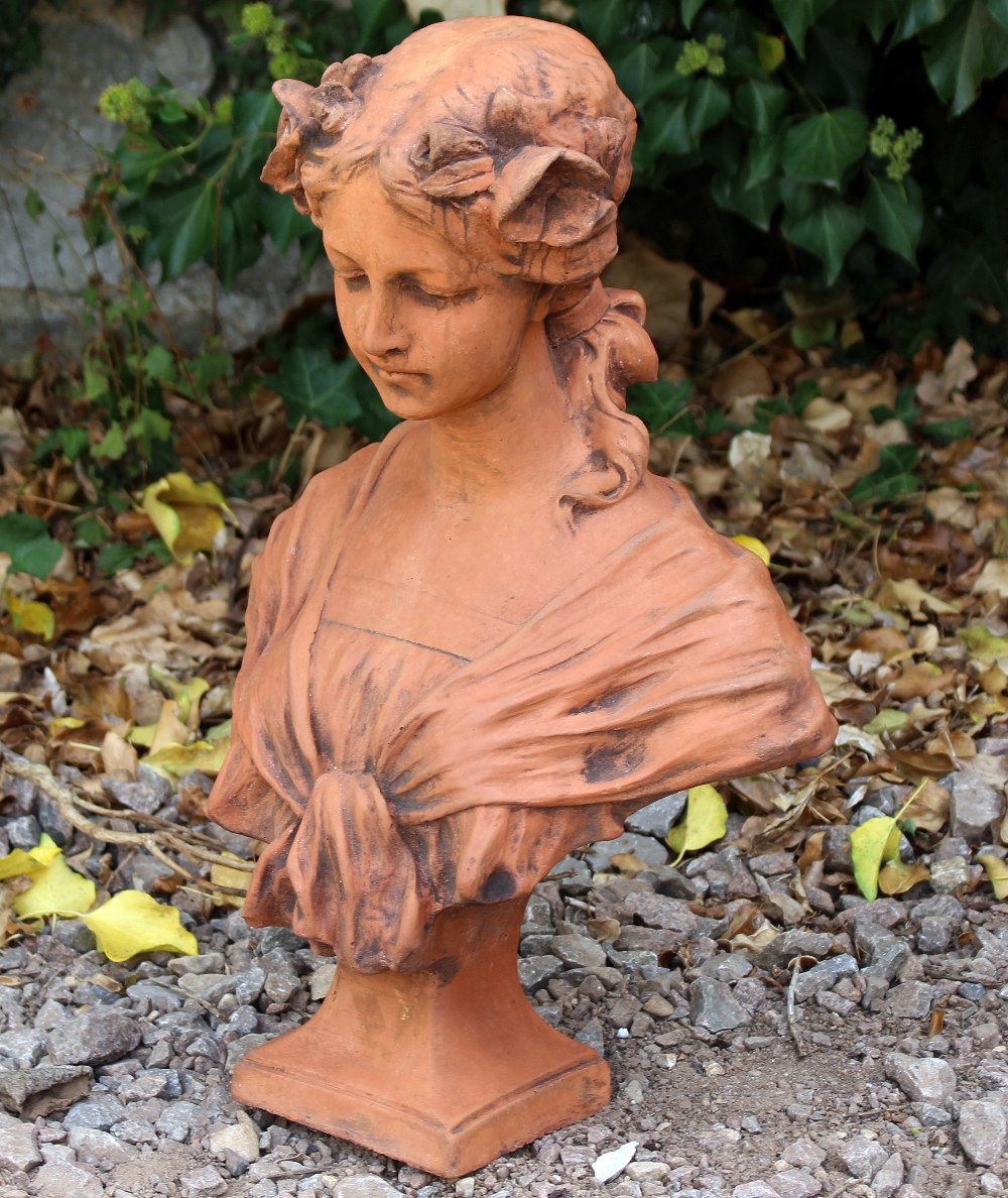 A CAST TERRACOTTA BUST OF AN ART NOUVEAU GIRL with flowers in her hair and on a square plinth