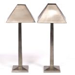 A PAIR OF BRUSHED STEEL TABLE LAMPS with conical shades, square section stems and spreading bases,