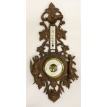 A CARVED WOOD BLACK FOREST HANGING ANEROID BAROMETER AND THERMOMETER decorated with a head of a