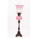A LATE 19TH CENTURY BRONZE OIL LAMP with a cranberry glass shade, duplex burner, pink glass well and
