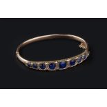 A SAPPHIRE AND DIAMOND SET BANGLE, of hinged oval form, applied with a tapered panel of graduated