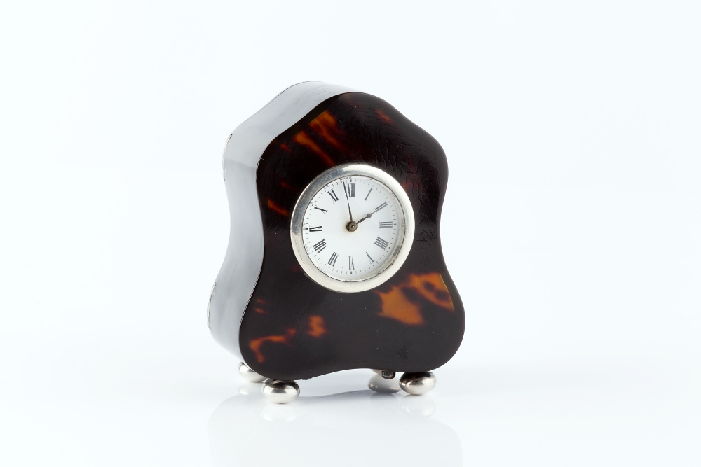 AN EARLY 20TH CENTURY SILVER MOUNTED TORTOISESHELL SMALL MANTEL TIMEPIECE, of shaped outline, with