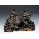 A SOUTH EAST ASIAN CARVED HARDWOOD GROUP of man on the back of a water buffalo on stand, 30cm wide x