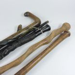 A collection of four various African carved wooden walking sticks, together with a baseball bat,