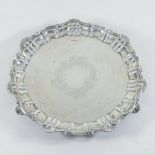 A George V silver salver, of circular shape with pie crust border, standing on four scrolled feet,
