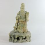 A Chinese carved green soapstone figure of an Emperor, shown standing holding a pomegranate,