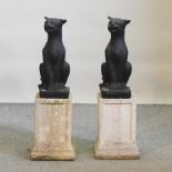 A pair of painted reconstituted stone models of cats, each on a pedestal base,
