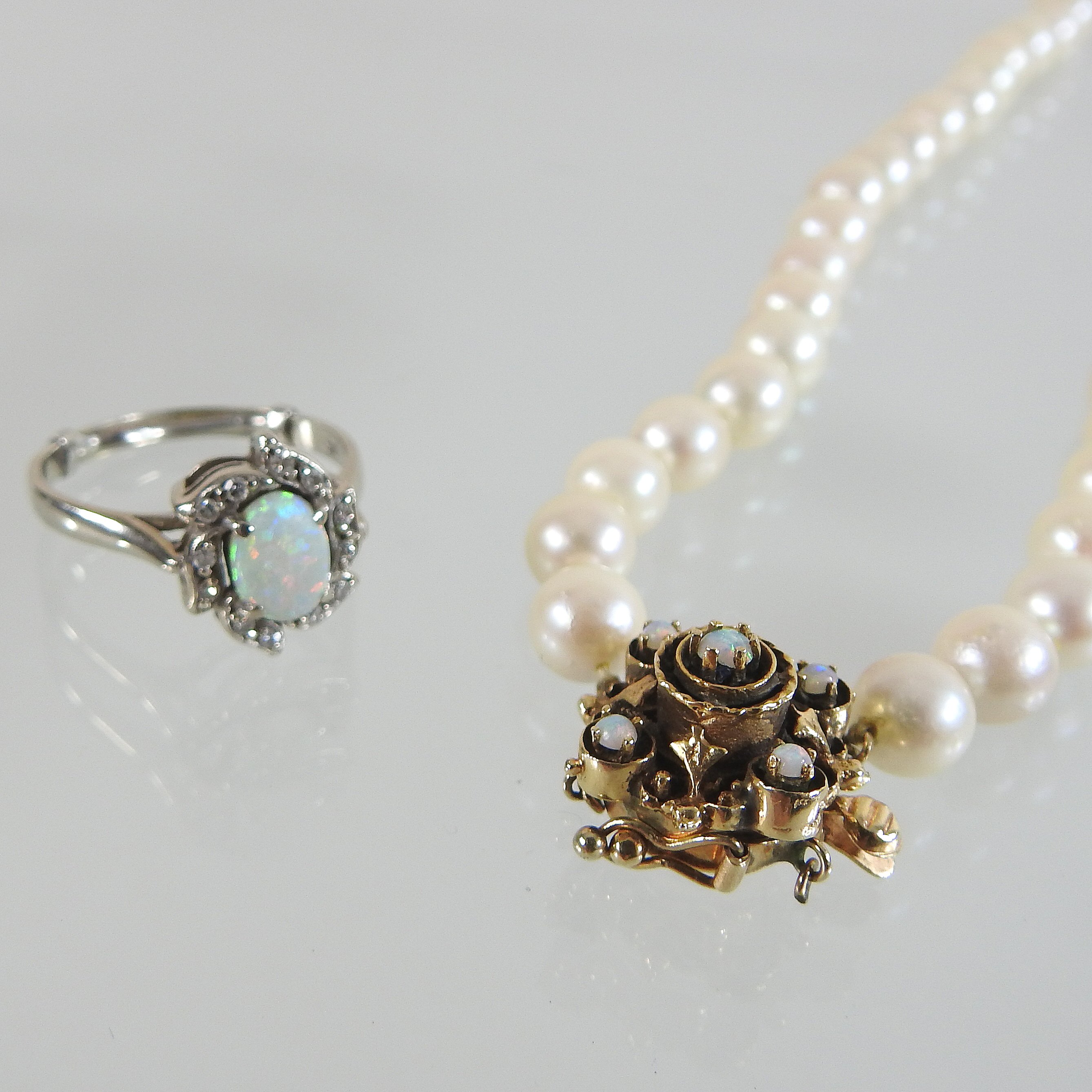 A 14 carat gold opal and diamond cluster ring, together with a cultured pearl single stand necklace,