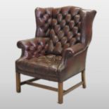 A Georgian style brown leather upholstered wing armchair, with a buttoned back and seat,