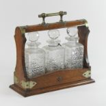 An Edwardian light oak and brass mounted tantalus, fitted with three cut glass decanters,