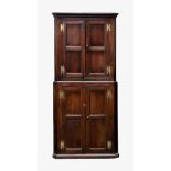 A George III joined oak two-part floor standing corner cupboard, the stepped pediment over a pair of