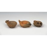 Three Grecian terracotta Hellenistic moulded oil lamps, the first of rounded form with concaved