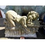 A composite stone garden ornament of a recumbent cherub72cm. long, 54cm. high, with attractive