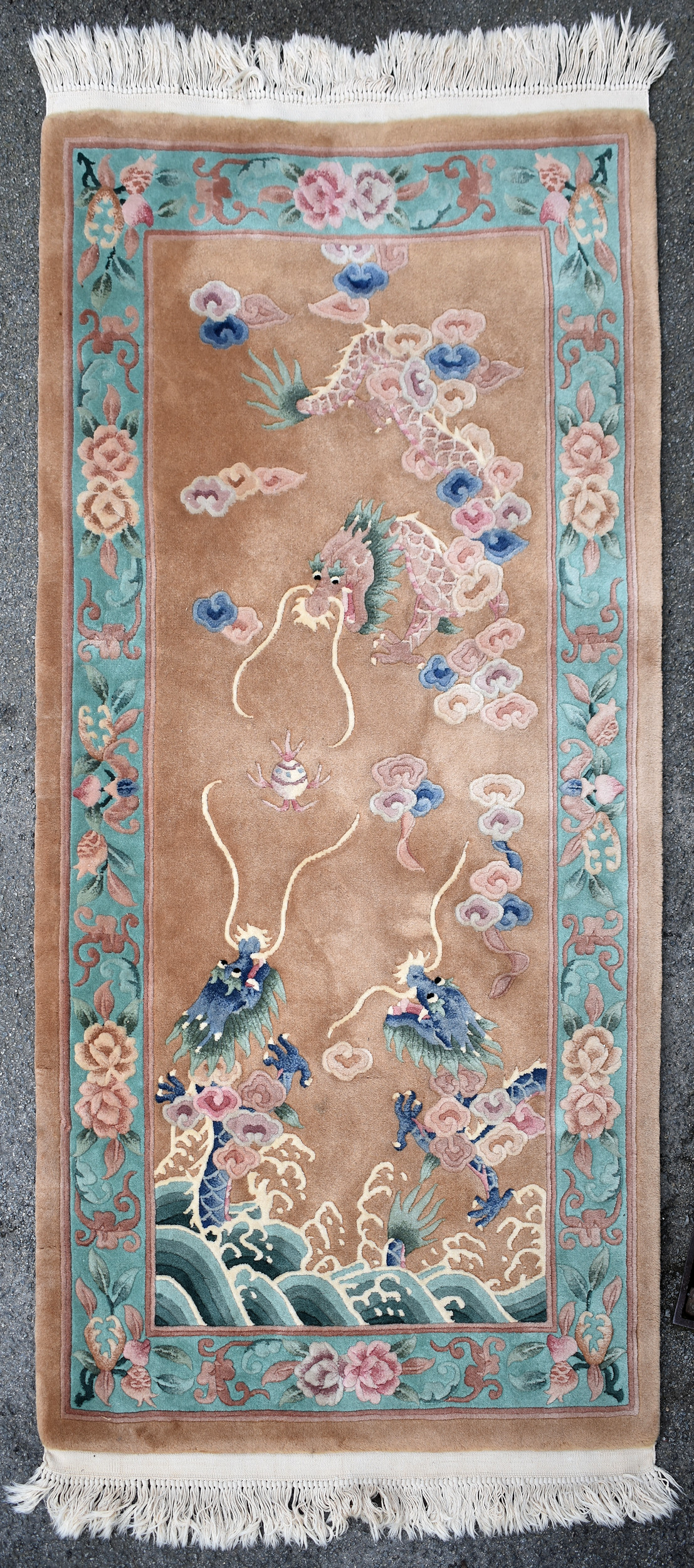 A Chinese wool dragon rug, mid-20th century, the buff ground with three pink, green and blue dragons