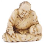 ˜LIGHTLY STAINED IVORY NETSUKE OF A MASK CARVER, CIRCA 1870 holding a mask of Hyottoko, his robe