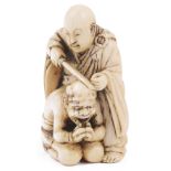 ˜IVORY NETSUKE OF A MONK SAWING OFF THE HORNS OF A PENITENT ONI, CIRCA 1870 signed: Tomochika 4.