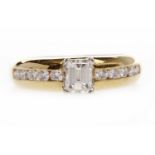 EIGHTEEN CARAT GOLD DIAMOND DRESS RING set with a central emerald cut diamond of approximately 0.