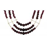 A SOUTH EAST ASIAN THREE STRAND NECKLACE OF GARNET BEADS, C MID 20TH C WITH WHITE METAL SPACERS,