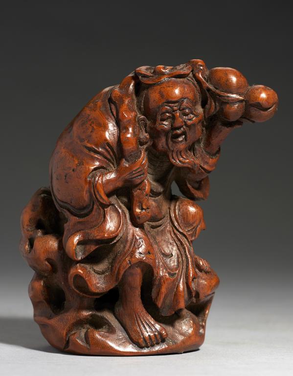 A CHINESE CARVED BAMBOO FIGURE OF SHOU-LAO on a rock, holding a peach bough in his left hand and