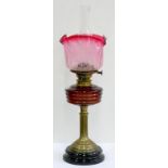 AN EDWARDIAN BRASS OIL LAMP, WITH REEDED PILLAR AND BASE, RUBY GLASS FOUNT, BRASS BURNER AND