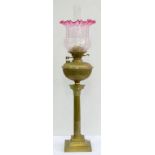 AN EDWARDIAN BRASS COLUMNAR OIL LAMP WITH REEDED BRASS FOUNT AND A CRANBERRY FLASHED AND MOULDED