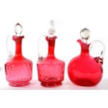 THREE VICTORIAN CRANBERRY GLASS CLARET JUGS AND VARIOUS CLEAR GLASS STOPPERS VARIOUS SIZES