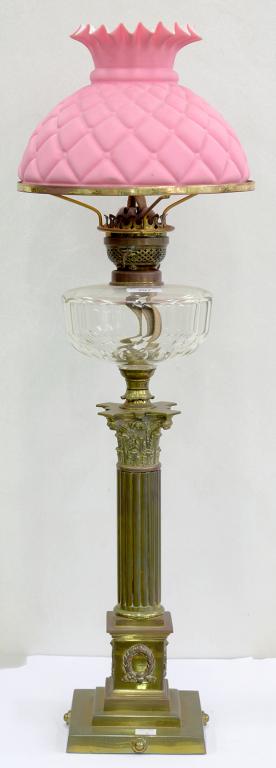 AN EDWARDIAN BRASS CORINTHIAN COLUMN OIL LAMP, WITH FACETED GLASS FOUNT AND BRASS BURNER, PINK