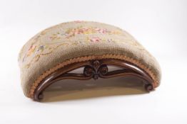 A Victorian curved footstool with needlework top and carved scroll and fleur de lys frame,