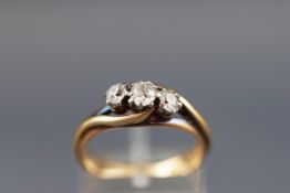 An early 20th century 18ct gold and diamond three stone cross-over ring, the old-cut stones approx.