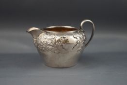 A late Victorian silver small round cream or milk jug with a scroll handle and part embossed with