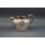 A late Victorian silver small round cream or milk jug with a scroll handle and part embossed with
