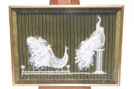 A lace and crochet picture of two peacocks mounted on a green striped fabric background,