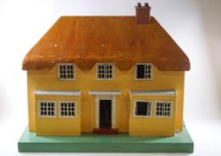 A 1950's dolls house in the form of a thatched cottage, 76cm wide,