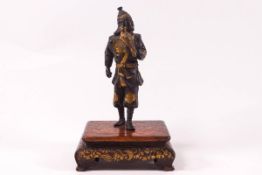 A Japanese Meiji period bronze figure holding a hawk on a hardwood stand, both highlighted in gilt,