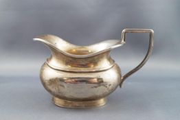 A silver oval cream or milk jug with an angular scroll handle and a bracket foot,