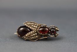 A Continental white metal, garnet cabochon and seed pearl brooch in the form of a winged insect,