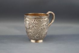 A Chinese export silver small mug with a scroll handle and profusely embossed with bamboo on a matt