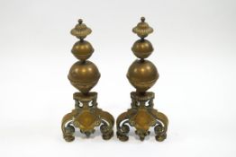 A pair of brass fire dogs, each with triple bulbous finials, on cartouche and scroll bases,